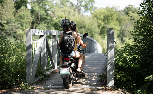Bild zeigt zwei Leute auf einem E-Moped über eine Brücke fahren